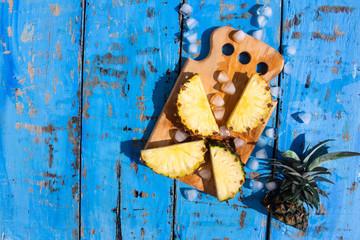 fresh pineapples  and ice cubes on cutting board isolated on a blue wooden background, copy space