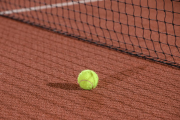 Tennis ball next to the net shot with a shallow depth of field on a clay court