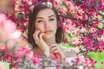 Beauty portrait. Young attractive woman with flowers. Closeup picture of beautiful lady outdoor on spring background. Pink petals.