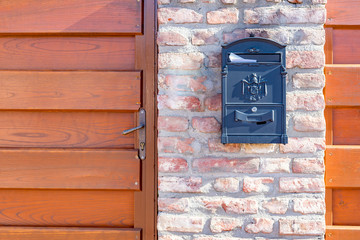 Black mail box with white letter on brick wall with wooden door