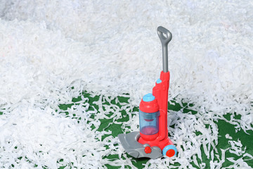 Children's toy plastic vacuum cleaner on green carpet with lots of paper white garbage
