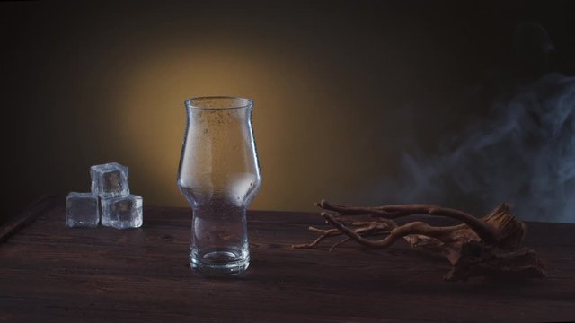 empty beer pint on a wooden table with ice, smoke rises against the background