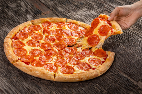 Hot pepperoni pizza ready to eat. Very cheesy pizza slice in hand on old wooden table - Powered by Adobe