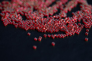 Transparent seed beads red color scattered on a dark background close-up