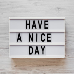 'Have a nice day' words on a lightbox on a white wooden background, top view. Overhead, from above, flat lay. Closeup.