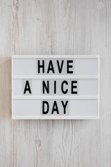 'Have a nice day' words on a lightbox on a white wooden background, top view. Overhead, from above, flat lay.