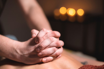 Close-up of the hands of a male masseur doing back massage to a girl at the spa. Low key high contrast shallow depth of field