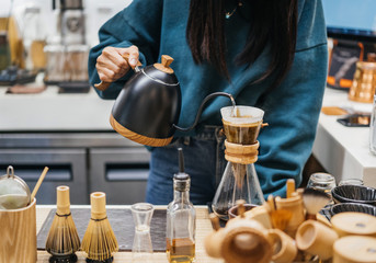 Barista pours boiling water from the kettle into a special paper filter in a cafeteria. Brewing coffee in an alternative way.