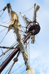 Masts and rigging of old pirate ship on background of cloudy blue sky