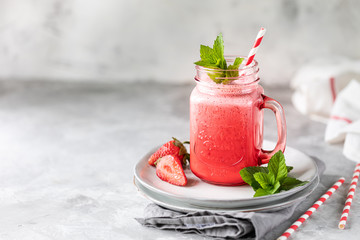 Strawberry and milk or yogurt smoothies in a beautiful red glass jar and sprigs of mint on a white concrete table. The recipe for the holiday Valentine's Day. Copy space