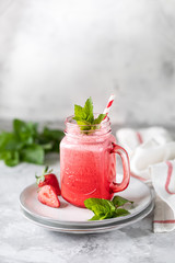 Strawberry and milk or yogurt smoothies in a beautiful red glass jar and sprigs of mint on a white concrete table. The recipe for the holiday Valentine's Day. Copy space