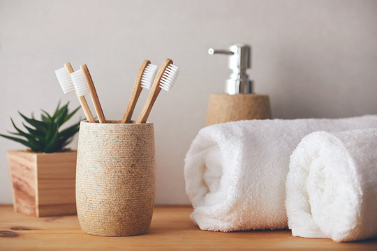 Four bamboo toothbrushes in a cup and white towels