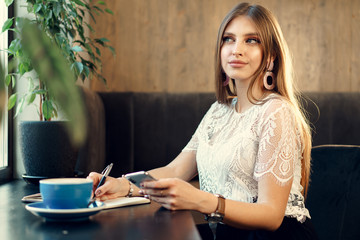 Young business woman sitting at the table in a coffee shop and making notes