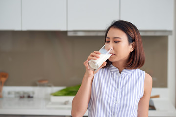Portrait of young Asian woman drinking milk while standing in the kitchen.