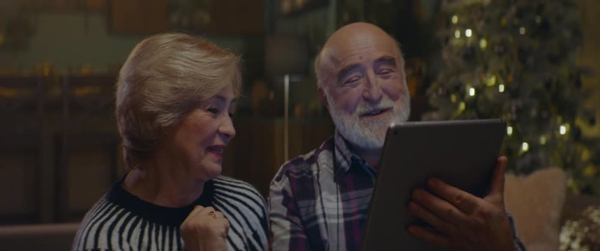 Senior adult Caucasian couple watching something on a portable tablet PC on Christmas Eve at their home. Shot on ARRI Alexa Mini with Cooke 2x Anamorphic lenses. 4K UHD RAW Graded footage