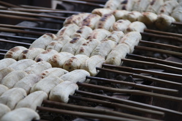 Row of peel off banana fruits are on bamboo skewer roasting on charcoal stove in Thailand.