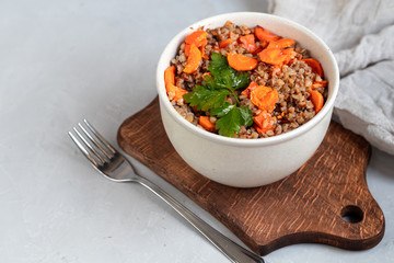 Buckwheat porridge in a bowl with stewed carrots. Decorated with green leaves. On a cotton napkin, on a light gray .