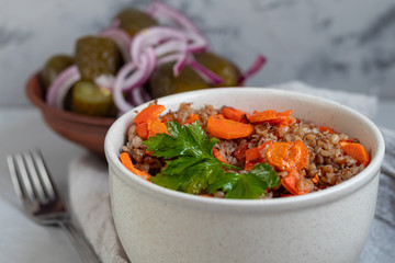 Buckwheat porridge in a bowl with stewed carrots. Decorated with green leaves. On a cotton napkin, on a light gray .