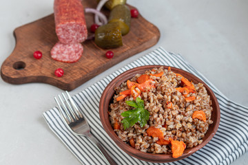 Buckwheat porridge in a bowl with stewed carrots. Decorated with green leaves. On a cotton napkin, on a light gray .