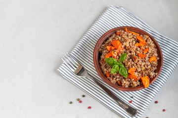 Buckwheat porridge in a bowl with stewed carrots. Decorated with green leaves. On a cotton napkin, on a light gray .