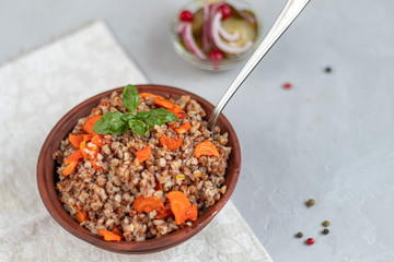 Buckwheat porridge in a bowl with stewed carrots. Decorated with green leaves. On a cotton napkin, on a light gray .