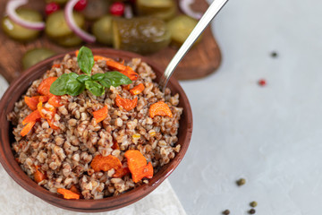 Buckwheat porridge in a bowl with stewed carrots. Decorated with green leaves. On a cotton napkin, on a light gray .