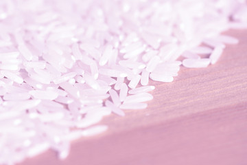 White rice grains scattered on a wooden surface close up. Food background pink color toned