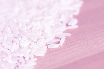 White rice grains scattered on a wooden surface close up. Food background pink color toned