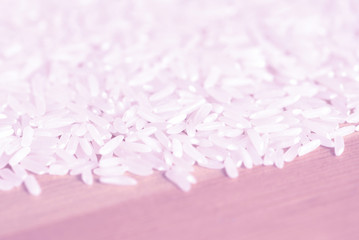 White rice grains scattered on a wooden surface close up. Food background pink color toned
