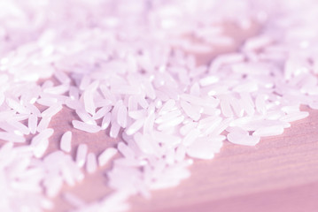 White rice grains scattered on a wooden surface close up. Food background pink color toned