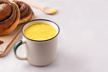 Indian turmeric drink with golden milk on a white plate next to buns with koice. Have copy space
