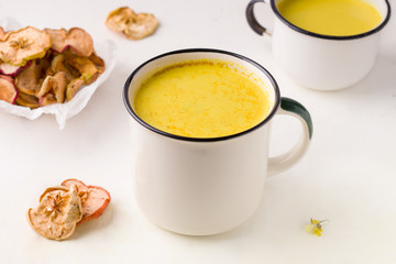 two mugs of golden milk next to healthy apple fruit chips on a white background