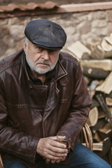 Obraz premium Elderly man with beard in leather jacket sits in yard