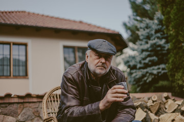 Elderly man with beard in leather jacket sits in yard