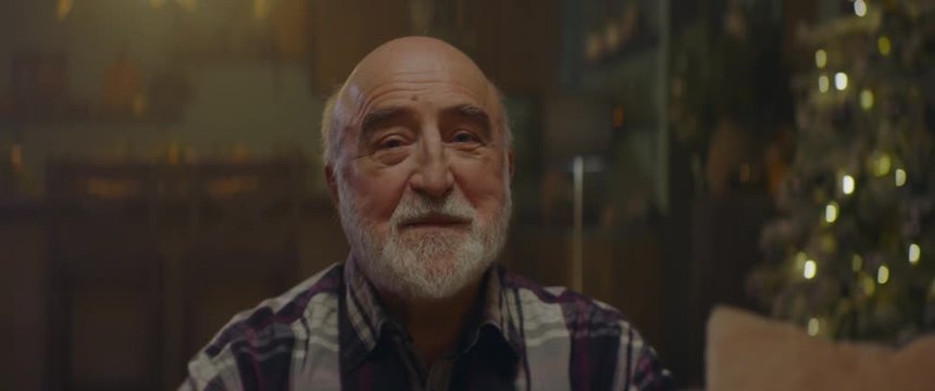 CU Portrait of good looking senior man looking and smiling into camera. Decorated Christmas interior in the background. Shot on ARRI Alexa Mini with Cooke 2x Anamorphic lenses. 4K UHD RAW Graded foota