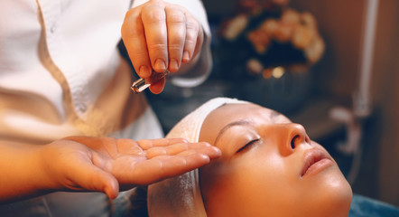 Close up hands of a female cosmetologist using an ampule product for skin care procedure on a womans face in a wellness spa center.