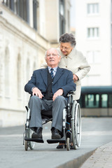 elderly woman pushing her handicapped husband on wheelchair