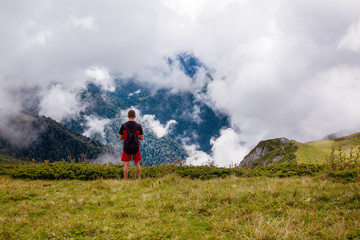 A traveler with a backpack on his shoulders standing on a mountain above the clouds.