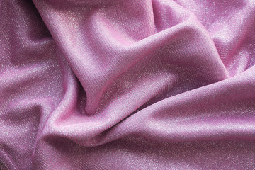 Background and texture of a pink shiny fabric lies with folds..