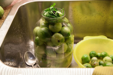 Large glass jar with green tomatoes stands in sink