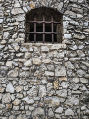 ancient stone wall with a window on which there are metal gratings