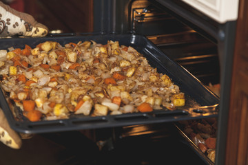Hands in mittens take out baking tray with vegetables oven