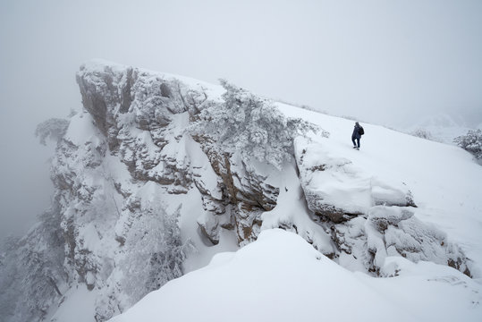 One man walks along the cliff to the top in the snowy misty mountains
