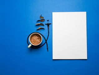 top view on white sheet book, coffee in white cup, green tree leaves, photo camera trigger, white work planning and life concept, classic blue 2020