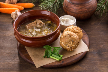 russian cabbage soup shchi with pork and cabbage in clay pot and bread bun on wooden table