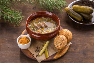 Pickled cucumber soup with pork and pearl barley and bread bun on wooden table