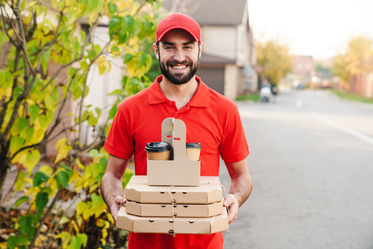 Image of smiling young delivery man holding pizza boxes and coffee