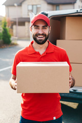 Image of smiling young delivery man standing with parcel box