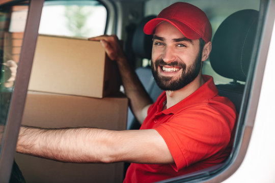 Image of happy young delivery man smiling and driving van