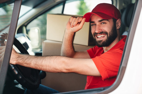 Image of happy bearded delivery man smiling and driving van